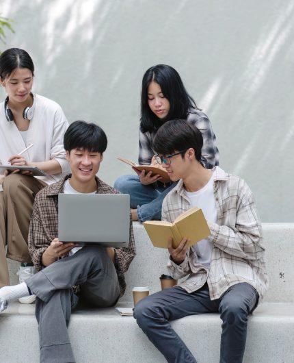 Group of Asian college student reading books and tutoring special class for exam on grass field at